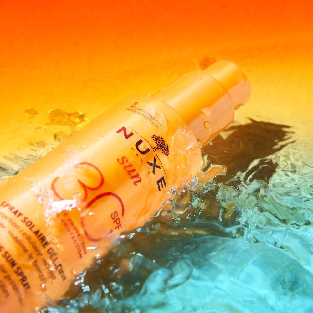 Sonnencreme-Flasche im Wasser. Aufschrift NUXE Sun, SPF 30. Spray Solaire Délicieux. Wasser spritzt.