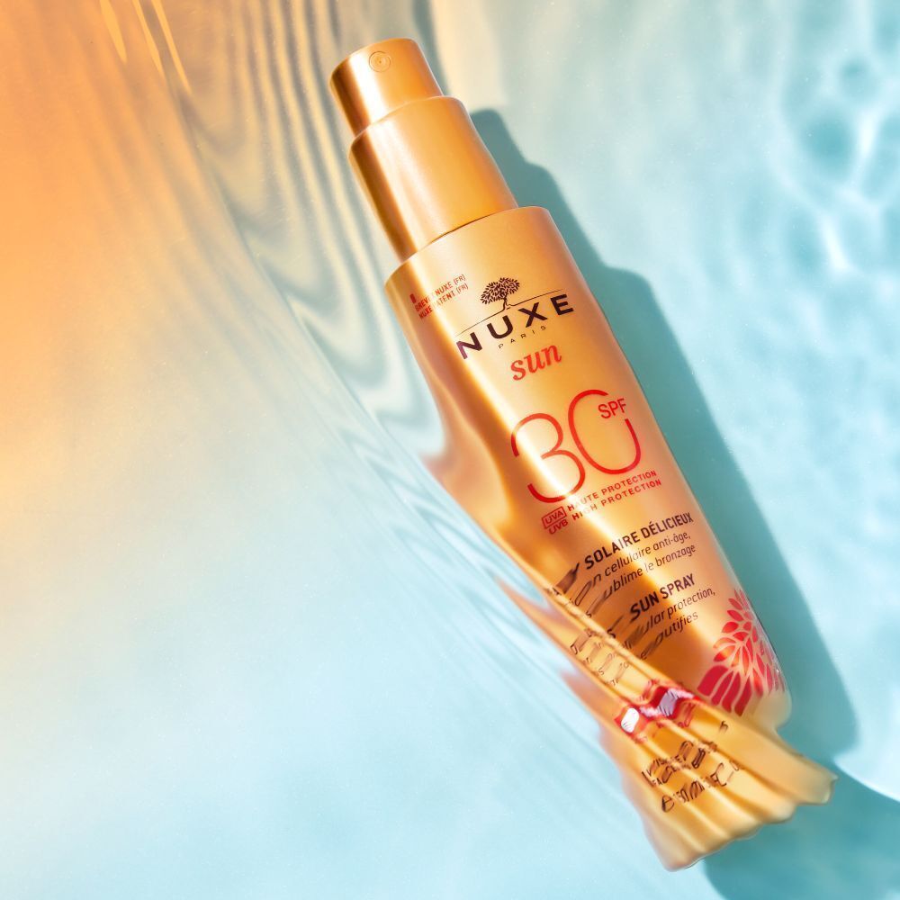 Sonnencreme-Flasche im Wasser. Aufschrift NUXE Sun, SPF 30. Text: Spray Solaire Délicieux.
