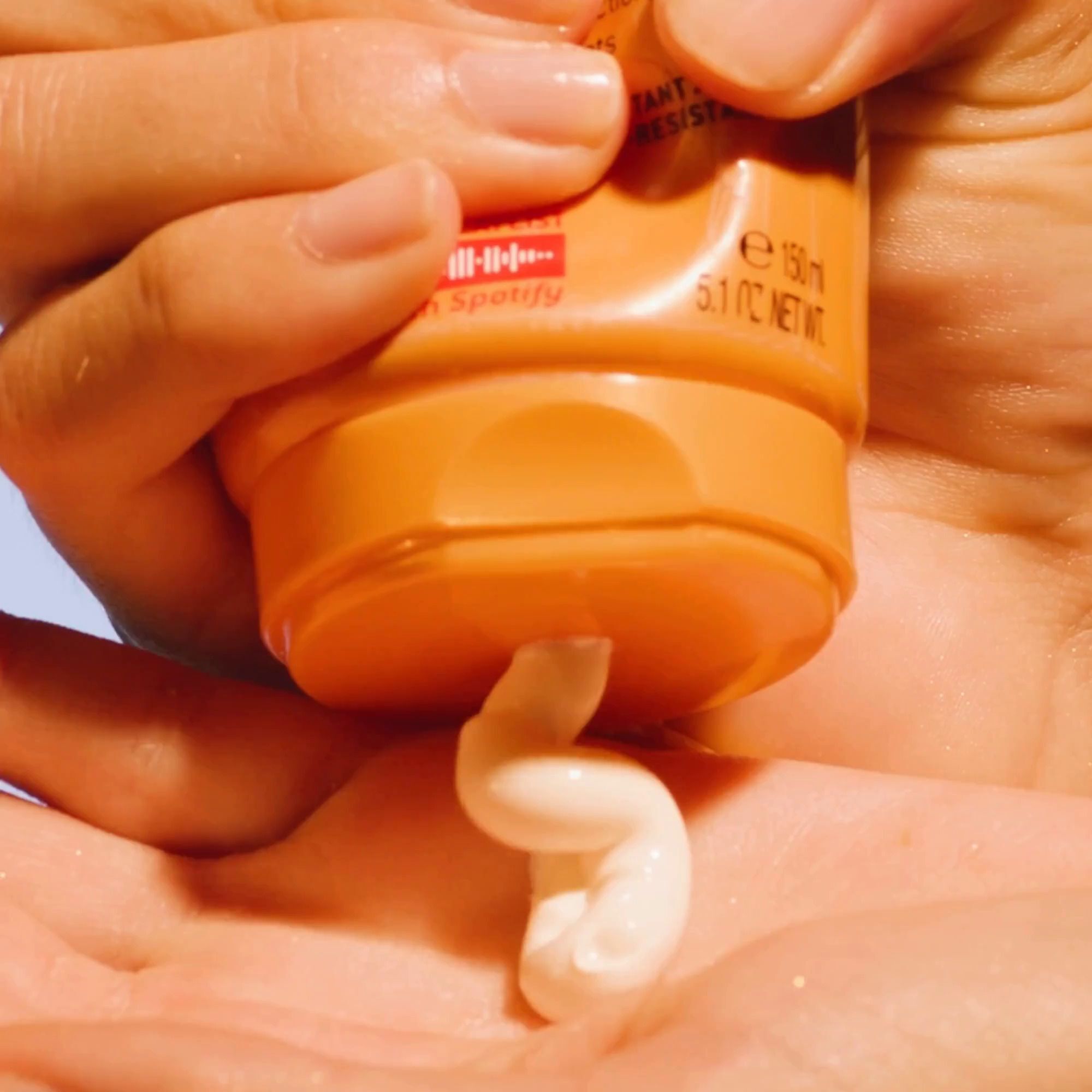 Hand hält Tube. Creme wird aus der Tube gedrückt. Produkt: Sonnenmilch.