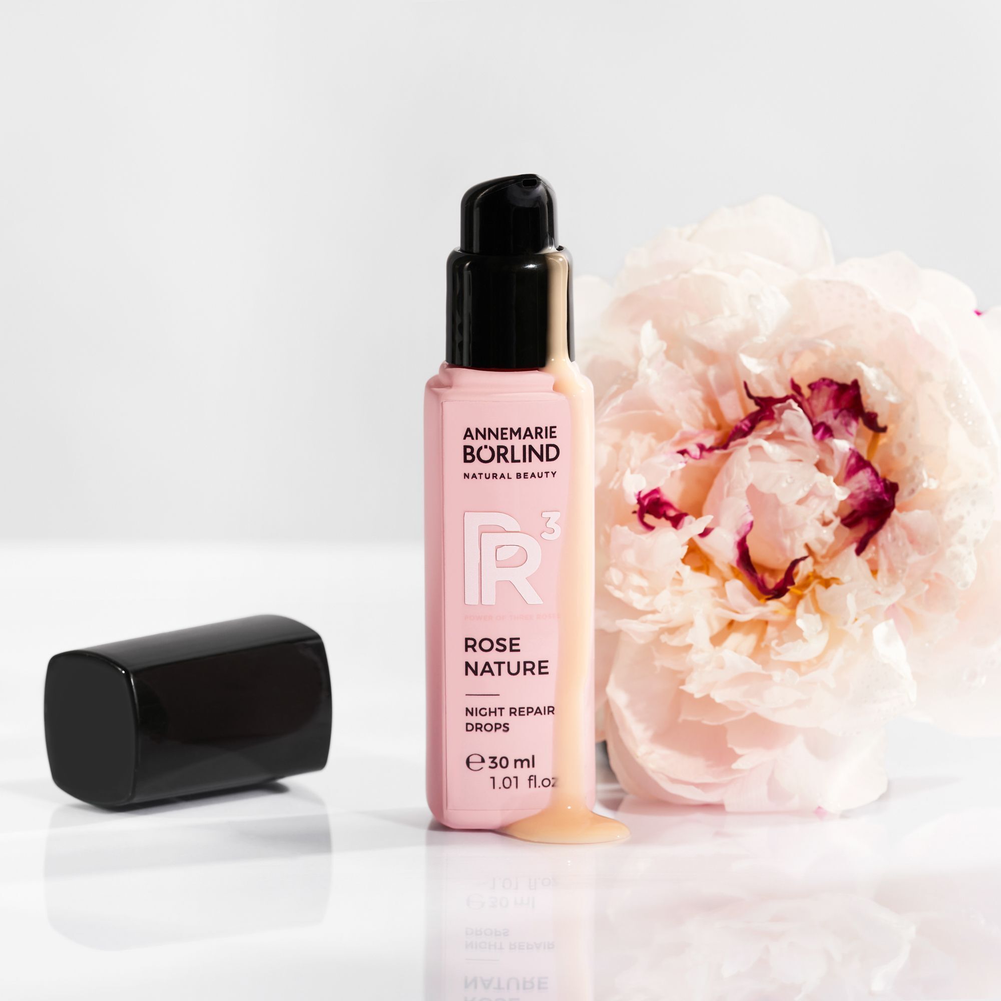 Eine Flasche ANNEMARIE BÖRLIND Rose Nature Night Repair Drops mit offenem Spender und einer Blüte.
