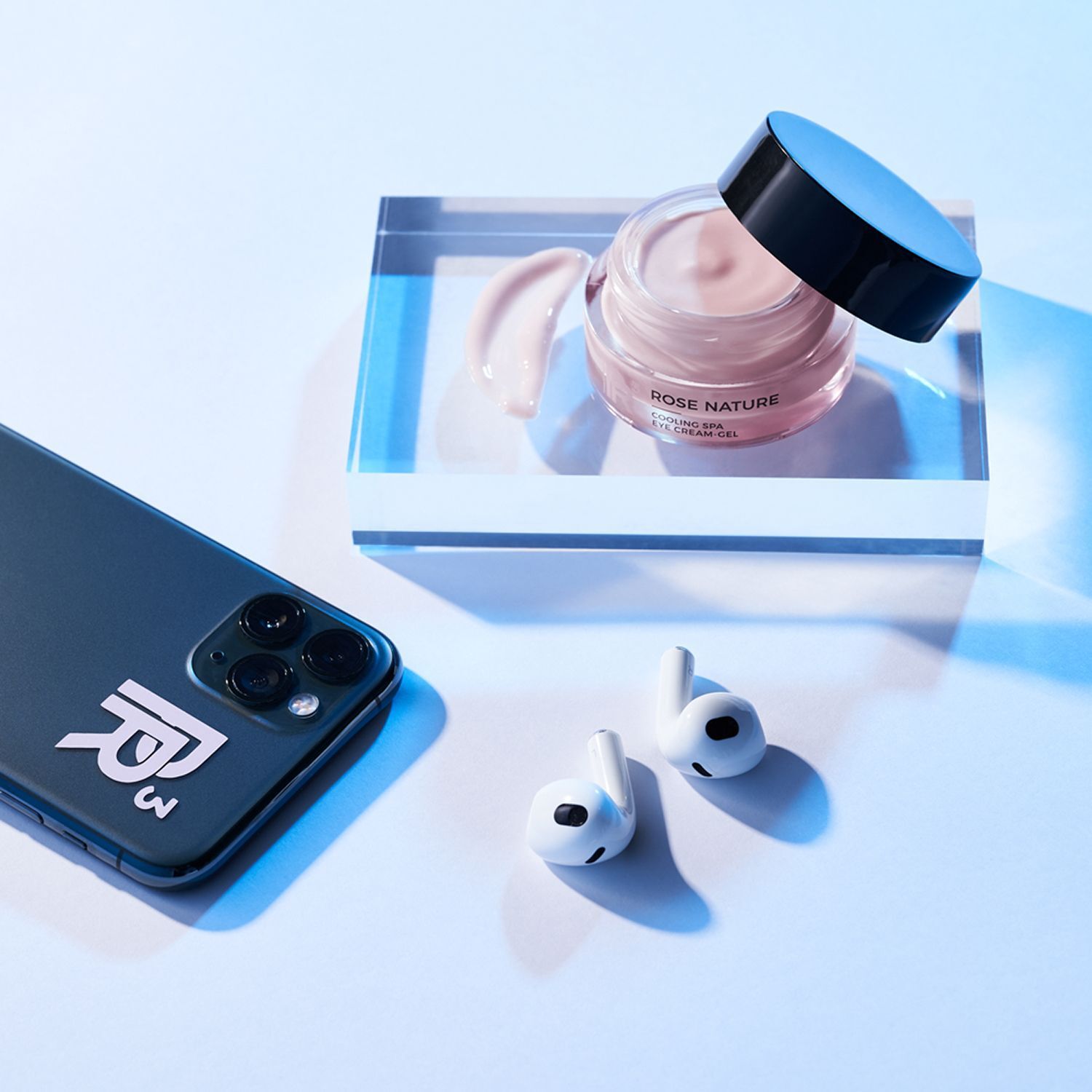 Tiegel ANNEMARIE BÖRLIND Rose Nature Cooling Spa Eye Cream Gel neben einem Smartphone und kabellosen Kopfhörern.