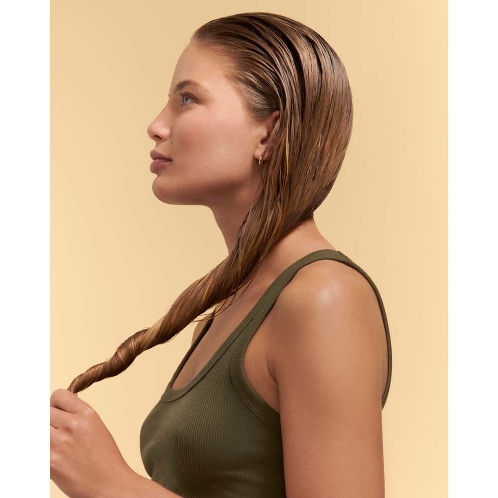 Profil einer Frau mit nassem Haar, das zu einem Zopf geflochten ist. Sie trägt ein olivgrünes Tanktop.