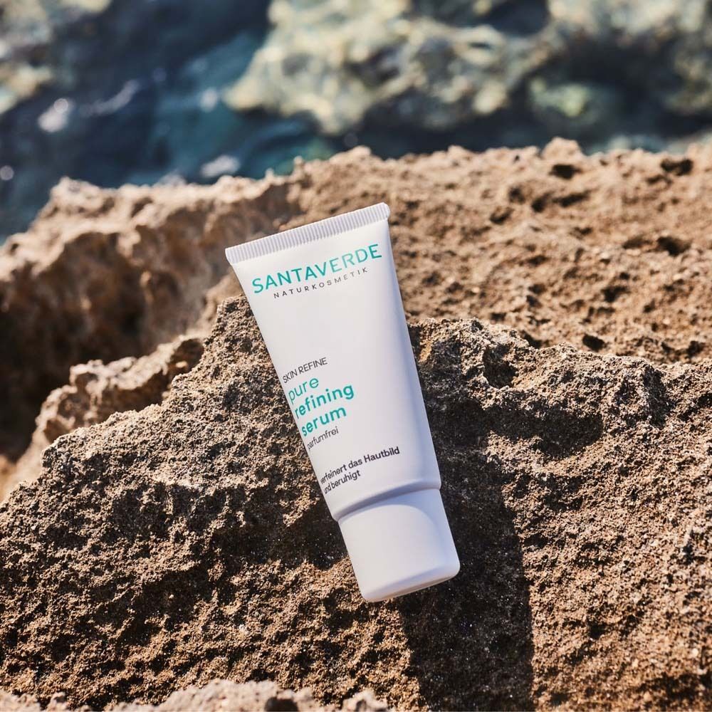 Eine Tube SANTAVERDE pure refining serum auf einem Felsen. Weiße Tube mit grüner Schrift. Aufschrift: Skin Refine, ohne Duft.