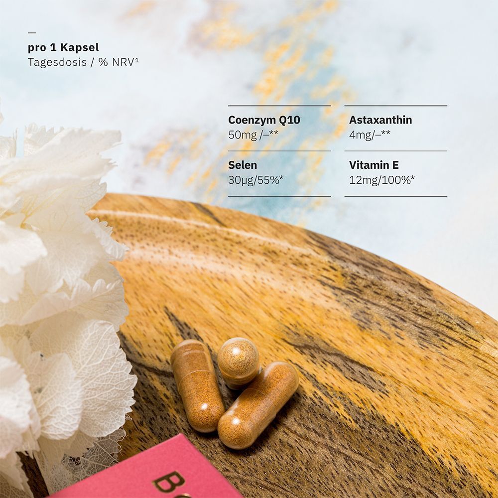 Kapseln auf Holz. Text: pro 1 Kapsel, Coenzym Q10, Astaxanthin, Selen, Vitamin E. Hintergrund: Blüten und verschwommener Hintergrund.