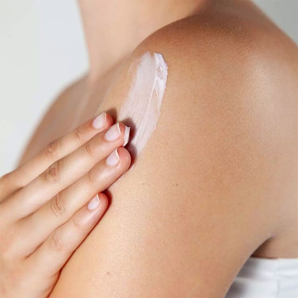 Nahaufnahme einer Person, die Creme auf die Schulter aufträgt. Weiße Creme auf der Haut. Helle Haut und Hintergrund.