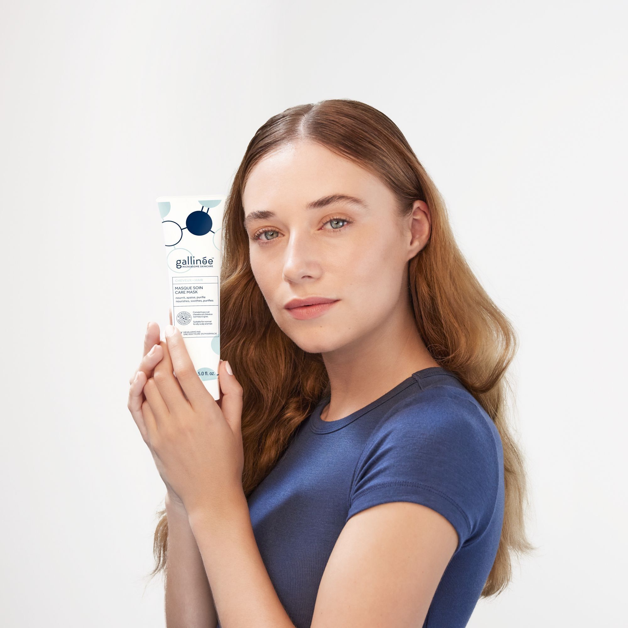 Eine Frau hält eine Tube Haarmaske. Marke: gallinée. Aufschrift: Masque Soin Care Mask. Die Frau hat lange, braune Haare.