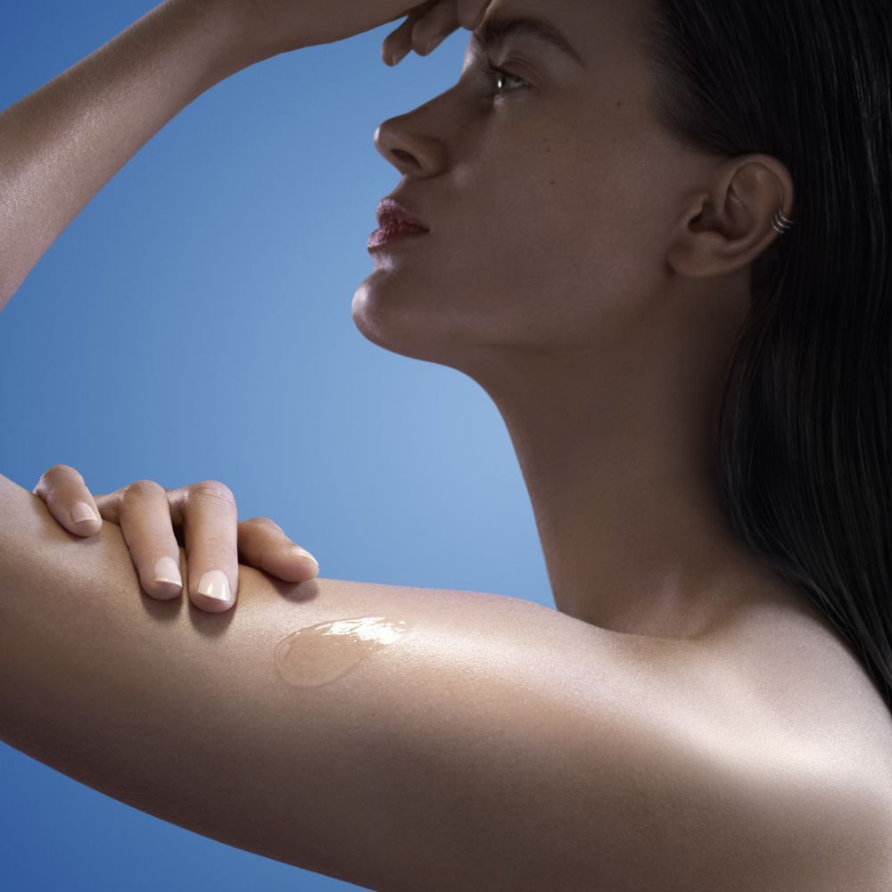 Eine Frau trägt eine transparente Gel auf ihre Schulter auf. Das Produkt ist sichtbar.