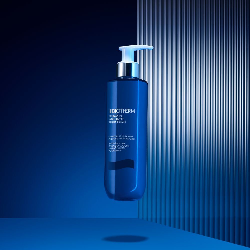 Eine blaue Flasche BIOTHERM Biocorps Anti-Bump Body Serum vor einem blauen Hintergrund mit vertikalen Linien.