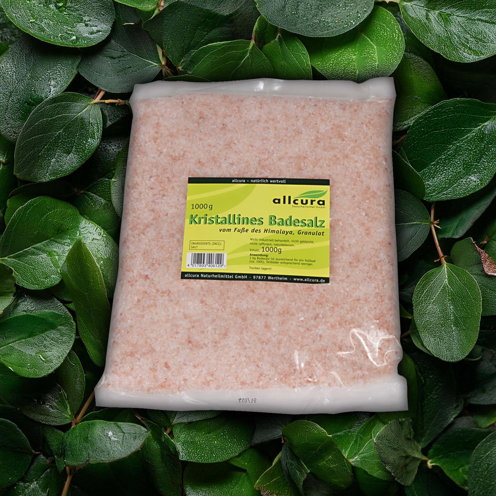 Ein Beutel mit rosafarbenem, kristallinem Badesalz. Aufkleber mit Produktinformationen und Logo. Hintergrund: grüne Blätter.