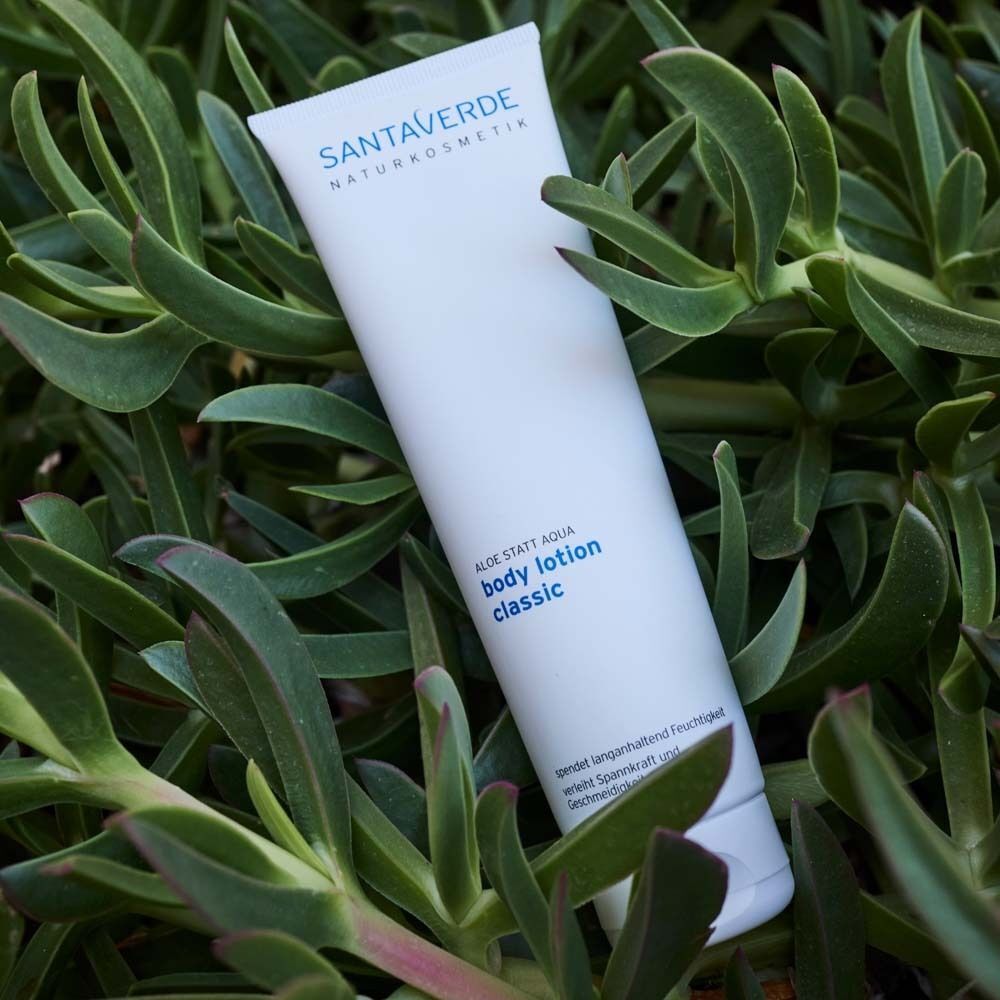 Weiße Tube mit SANTAVERDE-Logo und Aufschrift "body lotion classic" in grüner Umgebung.