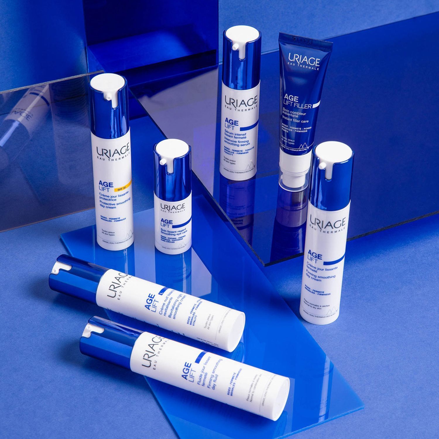 Mehrere weiße Flaschen und Tuben mit blauen Deckeln. Aufschrift: URIAGE AGE LIFT. Produkte auf blauem Hintergrund angeordnet.