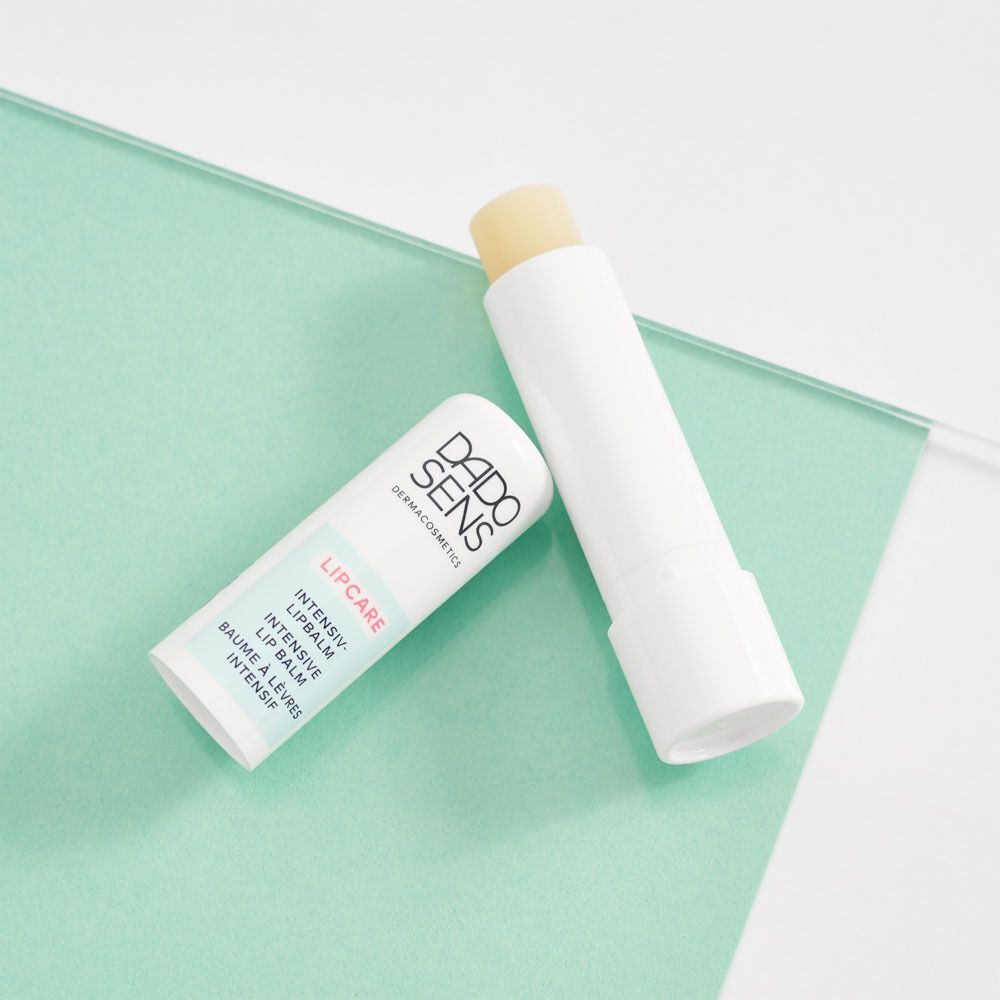 Zwei DADO SENS Intensiv-Lipbalm Stifte, einer geöffnet, auf einem mintgrünen Untergrund.