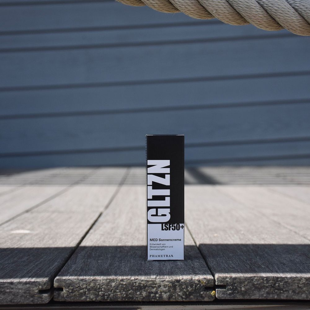 Verpackung der GLTZN MED Sonnencreme LSF 50+ auf Holzplanken am Strand.