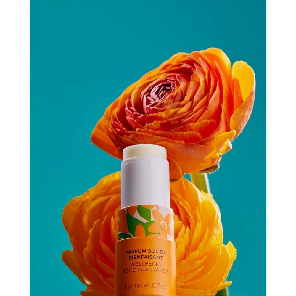 Zylindrischer Behälter mit geöffnetem Stift. Weiß mit orangefarbenem Band, floralem Muster. Marke Roger & Gallet. Vor orangefarbenen Blüten.