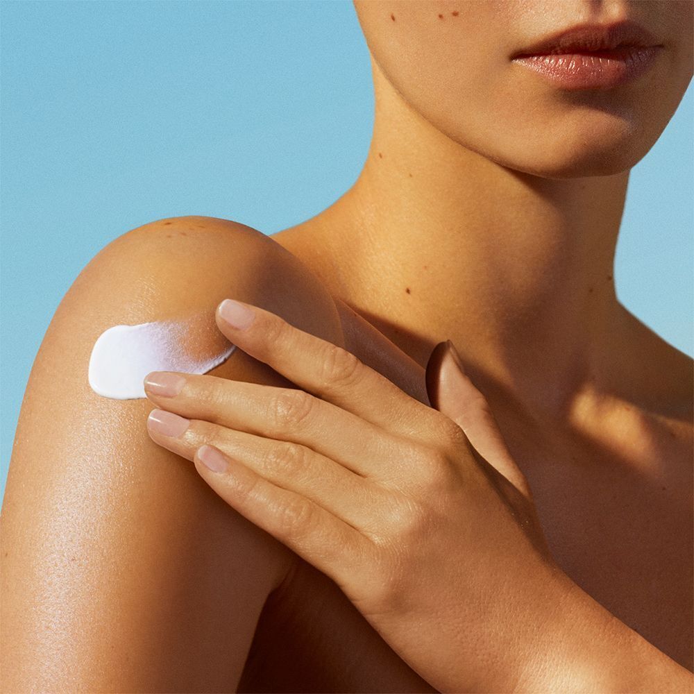 Nahaufnahme einer Person, die Sonnencreme auf die Schulter aufträgt. Weiße Creme auf der Haut.