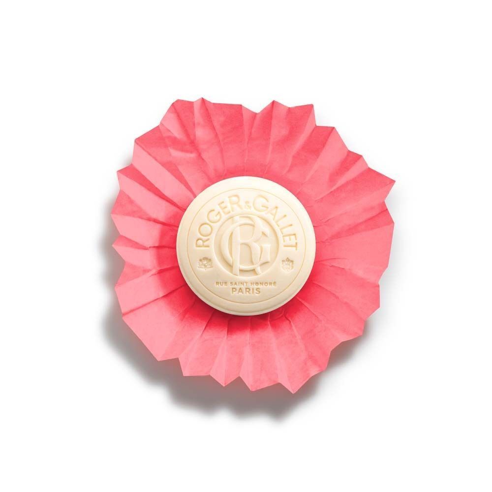 Eine runde, cremefarbene Seife in rosa Faltpapier. Das Logo von Roger & Gallet ist auf der Seife zu sehen.