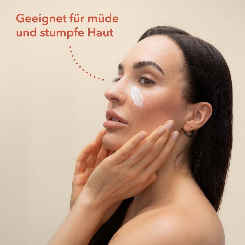 Frau mit Creme auf der Wange. Text: Geeignet für müde und stumpfe Haut.