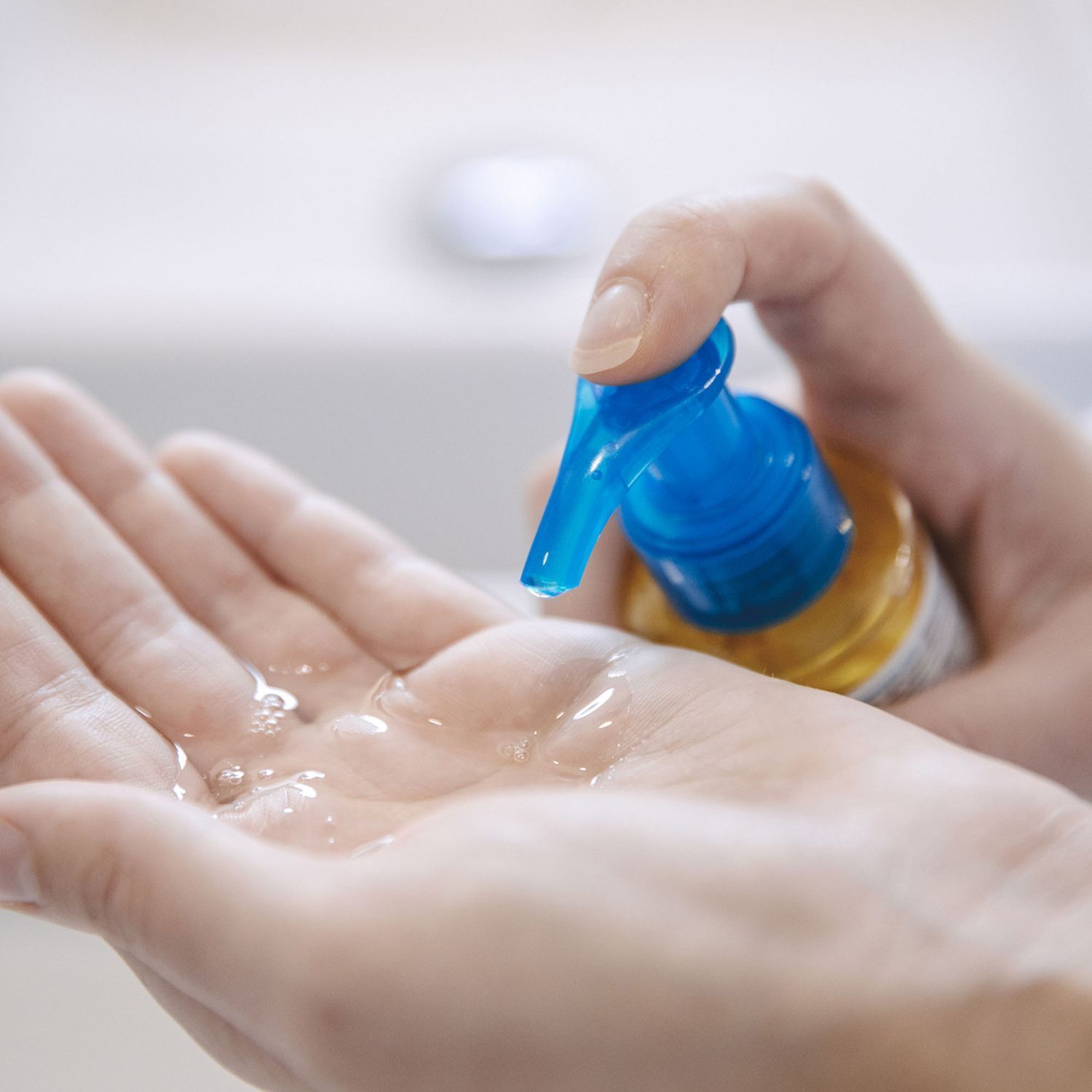 Hand drückt Flüssigkeit aus einer Flasche mit blauem Pumpkopf. Flüssigkeit in der Handfläche. Hintergrund: Waschbecken.