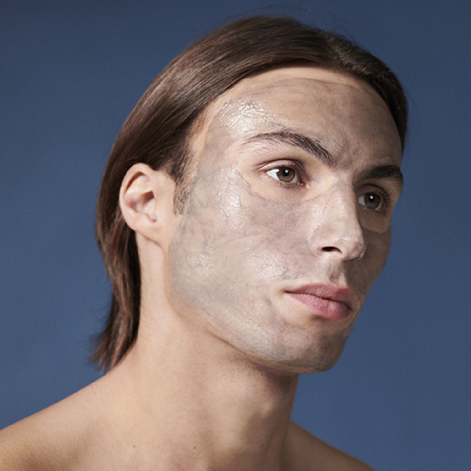 Ein Mann mit einer Gesichtsmaske. Die Maske ist grau und bedeckt das Gesicht. Blauer Hintergrund.