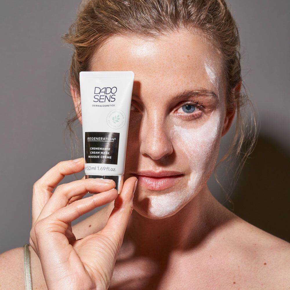 Frau hält eine Tube DADO SENS REGENERATION Crememaske vor ihr Gesicht.