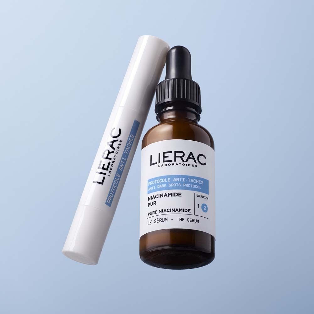 Weißer Stick und braune Flasche mit Pipette. Aufschrift: LIERAC, Protocole Anti-Taches, Le Serum, Pure Niacinamide.