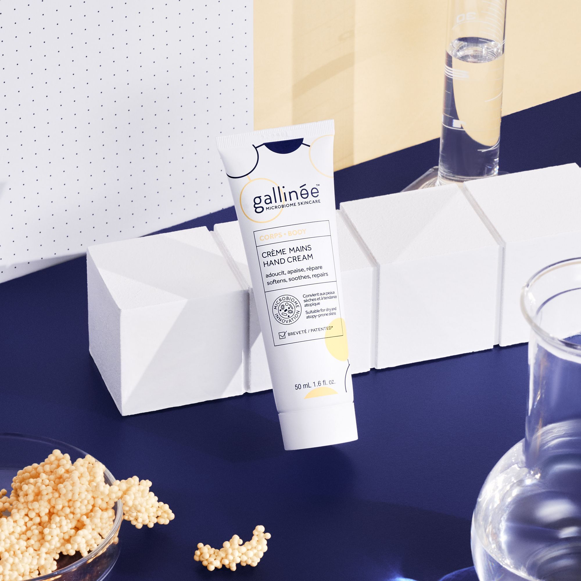 Eine Tube Handcreme vor geometrischen Blöcken. Aufschrift: gallinée, Crème Mains Hand Cream. Auf blauem Hintergrund, mit Zubehör.
