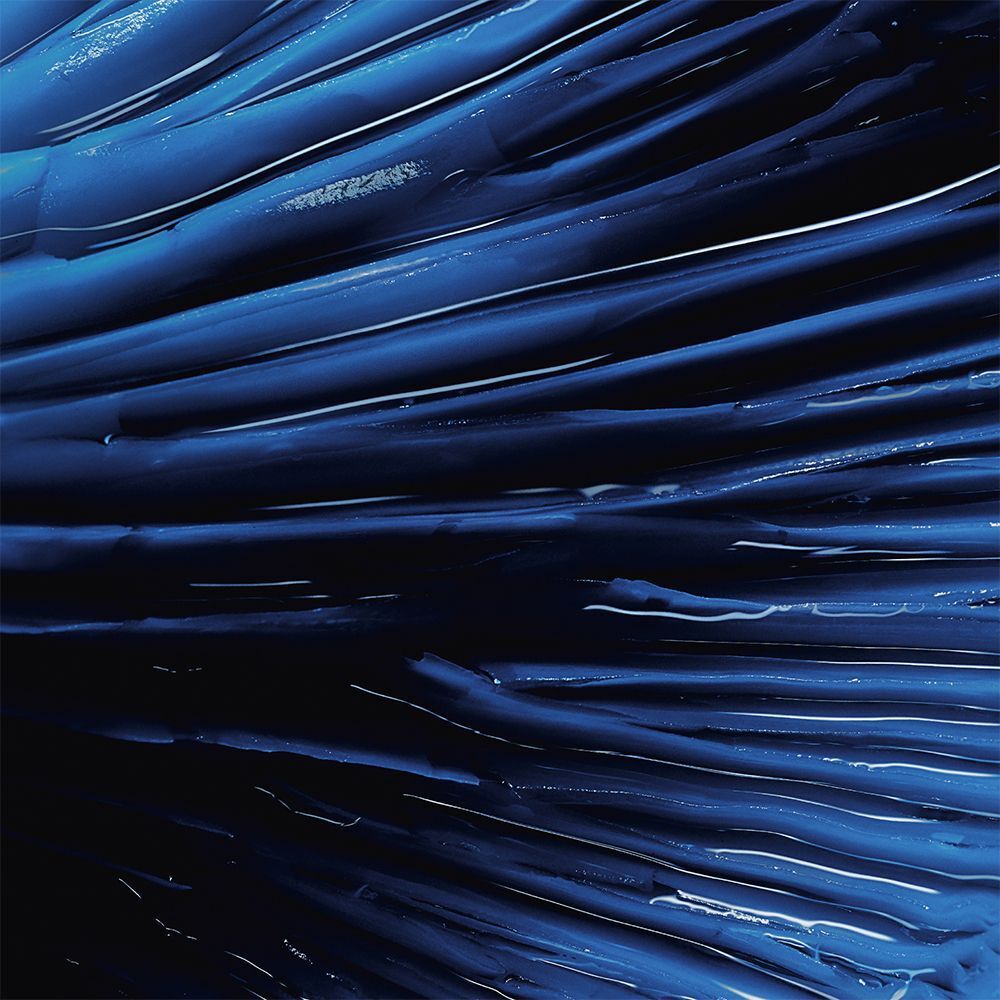 Nahaufnahme einer blauen, wellenförmigen Substanz. Glänzende Textur mit weißen Reflexen. Dunkler Hintergrund.