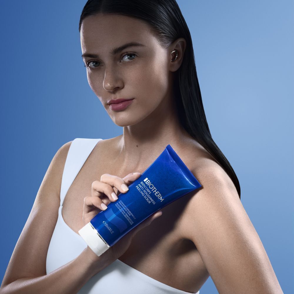 Frau hält blaue Tube BIOTHERM Biocorps Anti-Roughness Peeling Scrub. Sie trägt ein weißes Top.