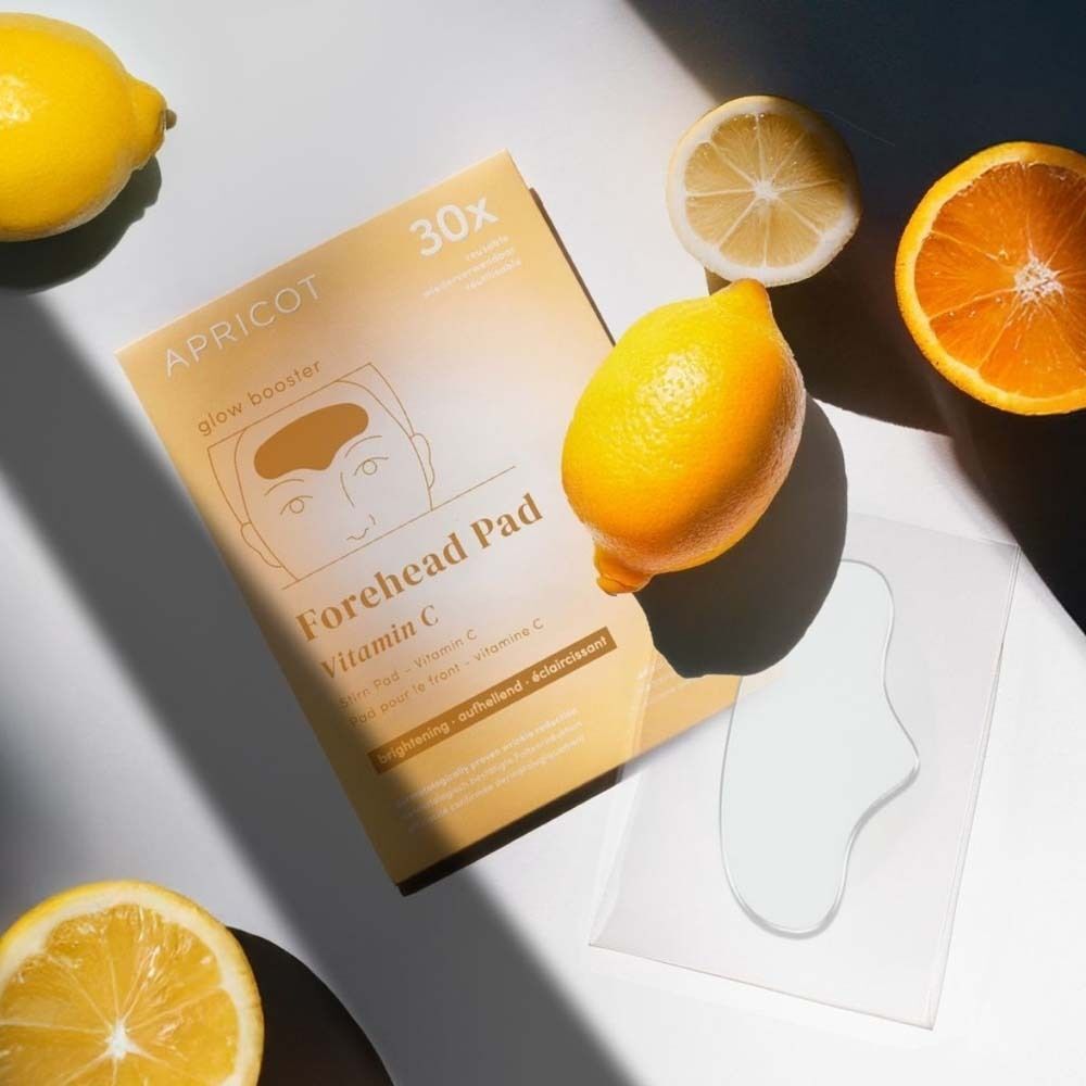 Verpackung mit Stirn Pad, daneben Zitronen und Orangen. Aufschrift: APRICOT, Forehead Pad, Vitamin C.