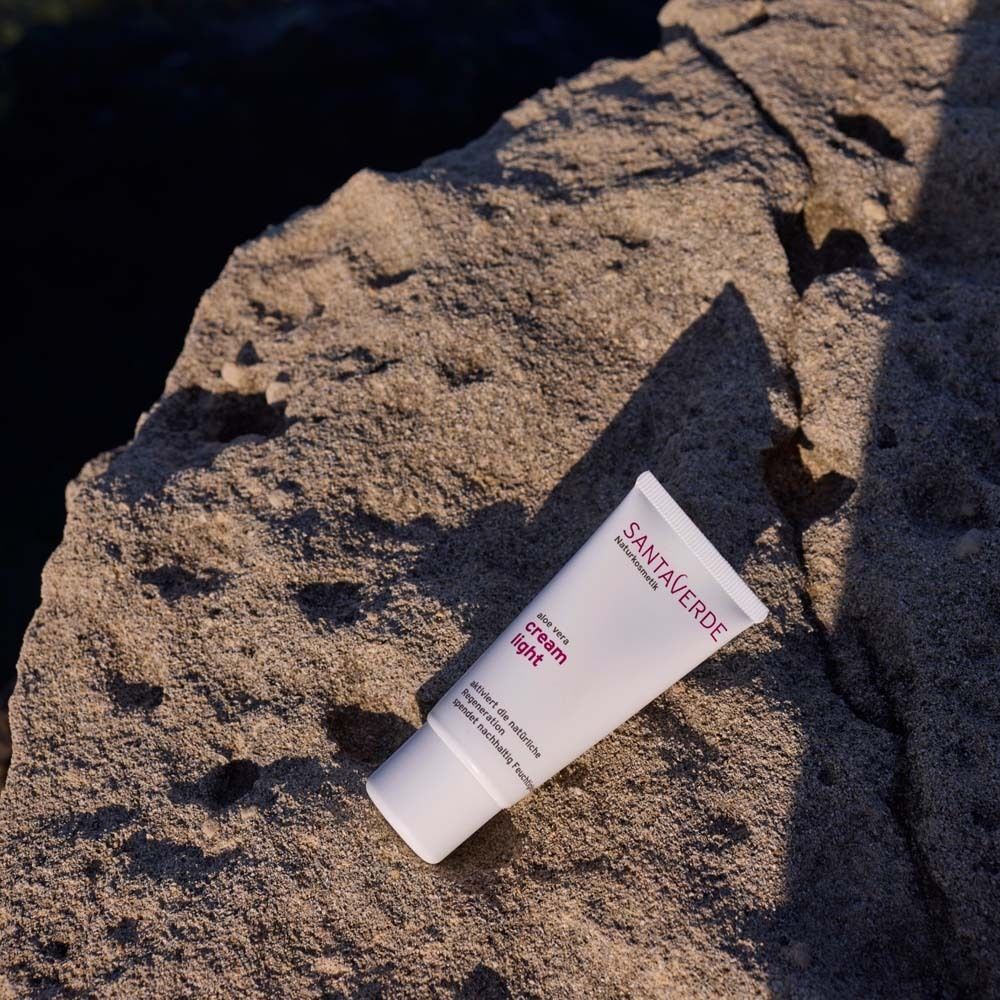 Eine Tube SANTAVERDE Creme Light auf einem Stein. Weiße Tube mit lila Schriftzug. Aufschrift: Face Care cream light.