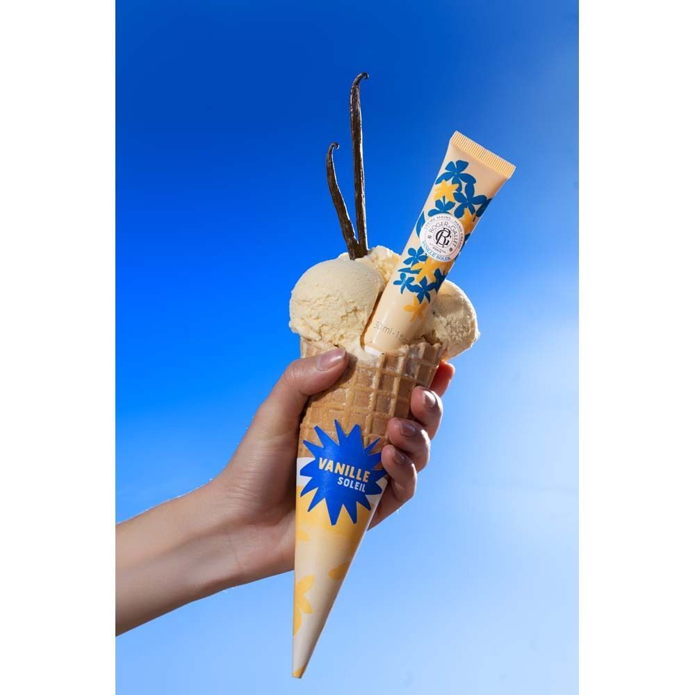 Hand hält Eistüte mit Eiscreme, Vanilleschoten und Handcreme-Tube. Aufschrift: Vanille Soleil.