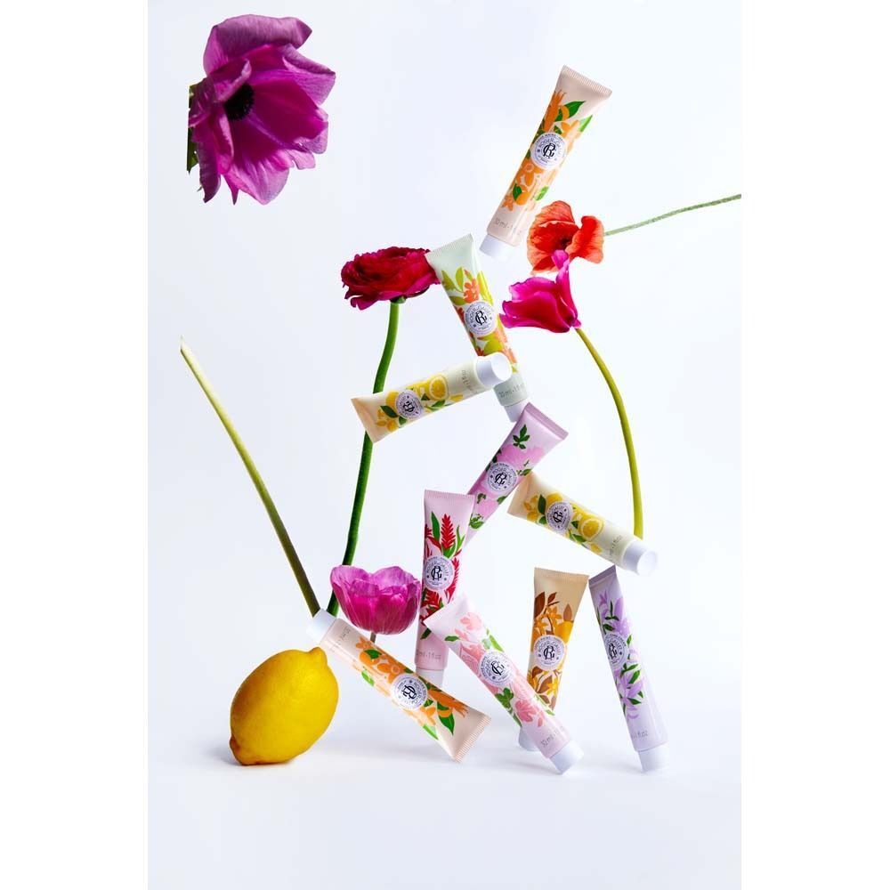 Mehrere Tuben Handcreme, arrangiert mit Blumen und einer Zitrone. Verschiedene Farben und Designs. Keine Produktnamen sichtbar.