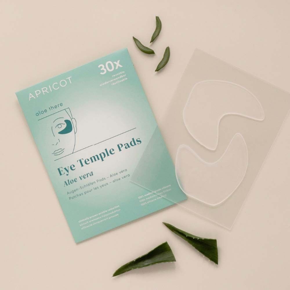 Verpackung mit Augen-Schläfen Pads, daneben Aloe Vera Blätter und Pads. Aufschrift: APRICOT, 30x, Eye Temple Pads, Aloe vera.