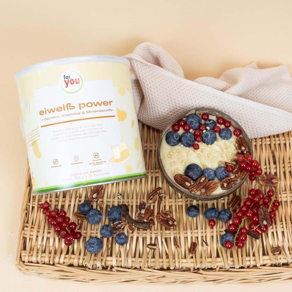 Dose 'For you' Eiweiß Power Vanille neben einer Schale mit Beeren und Nüssen auf einem Korb. Aufschrift: Carnitin, Vitamine & Mineralstoffe.