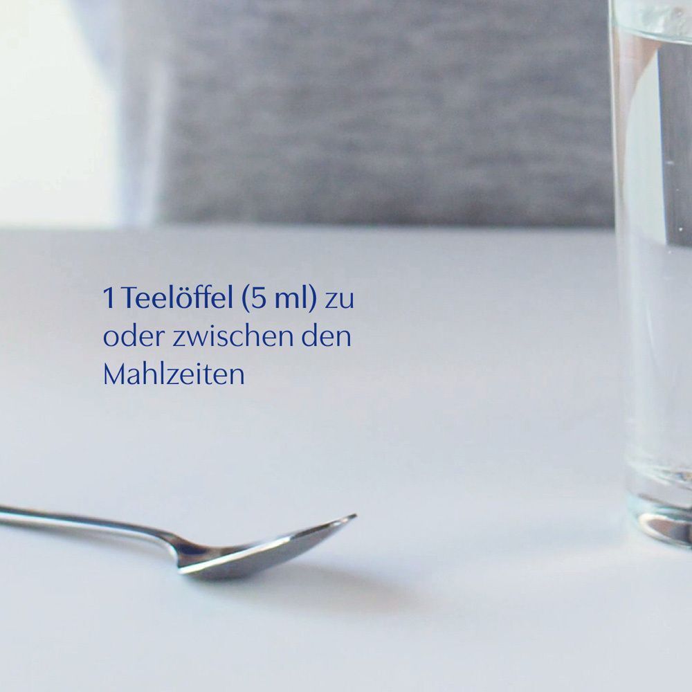 Ein Löffel neben einem Glas Wasser. Text: 1 Teelöffel (5 ml) zu oder zwischen den Mahlzeiten.