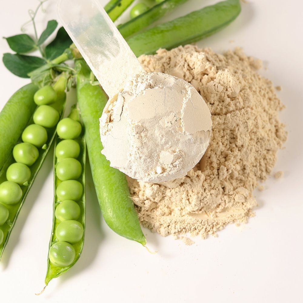 Proteinpulver auf einem Löffel, Erbsen und Blätter. Proteinpulver in einem Löffel. Grüne Erbsen und Blätter.