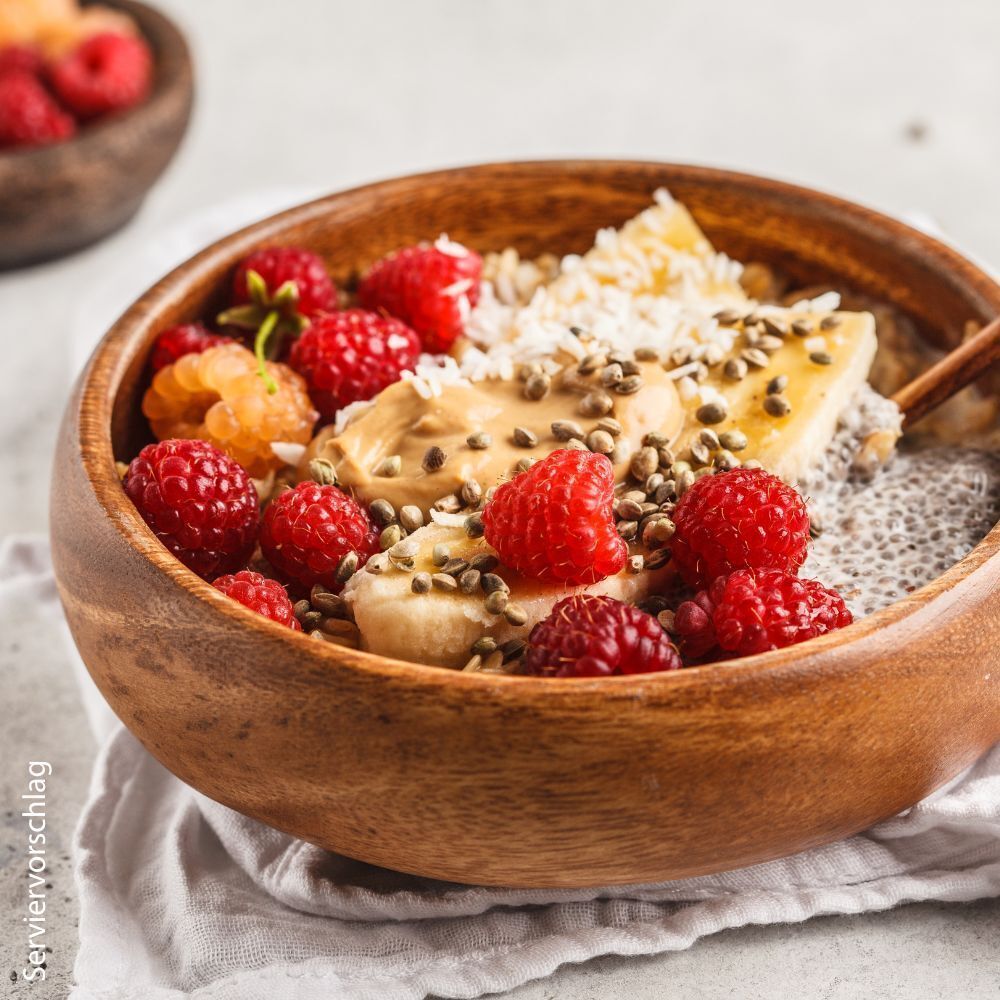 Schüssel mit Essen. Himbeeren, Bananenscheiben, Samen, Erdnussbutter. Servierbeispiel.