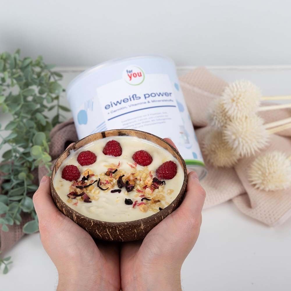 Eine Dose „for you eHealth Eiweiß Power Pur“ neben einer Kokosnussschale mit Himbeeren und Getreide. Hände halten die Schale.