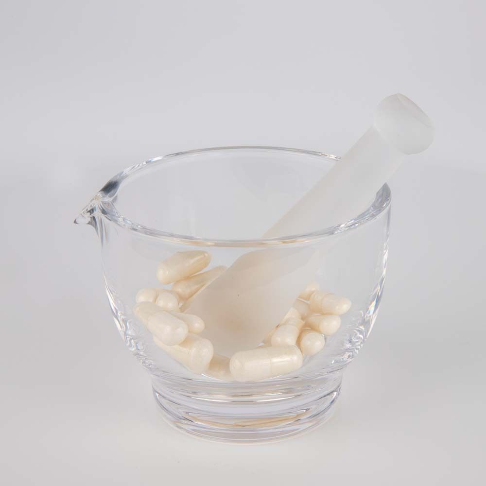 Glasmörser mit Stößel und Kapseln. Kapseln sind hellbeige. Mörser und Stößel sind weiß.