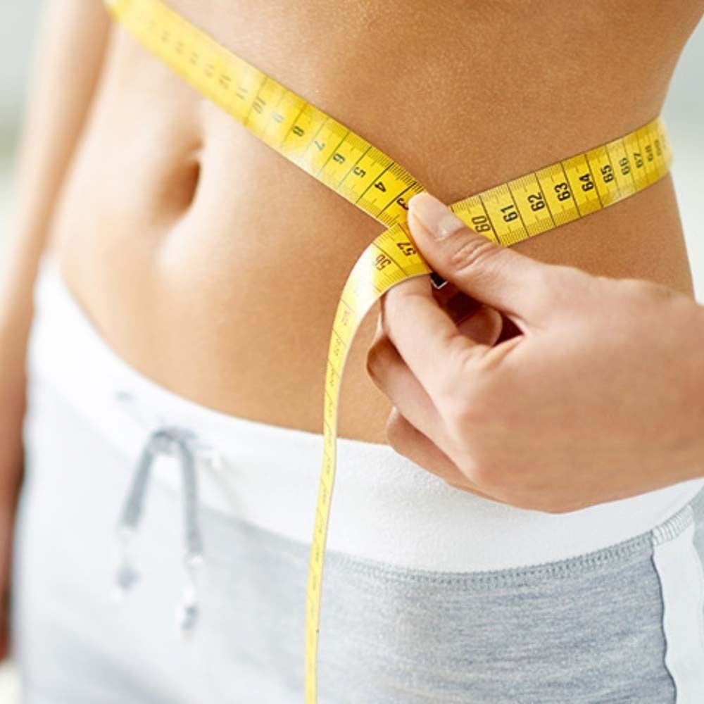 Eine Person misst ihre Taille mit einem gelben Maßband.