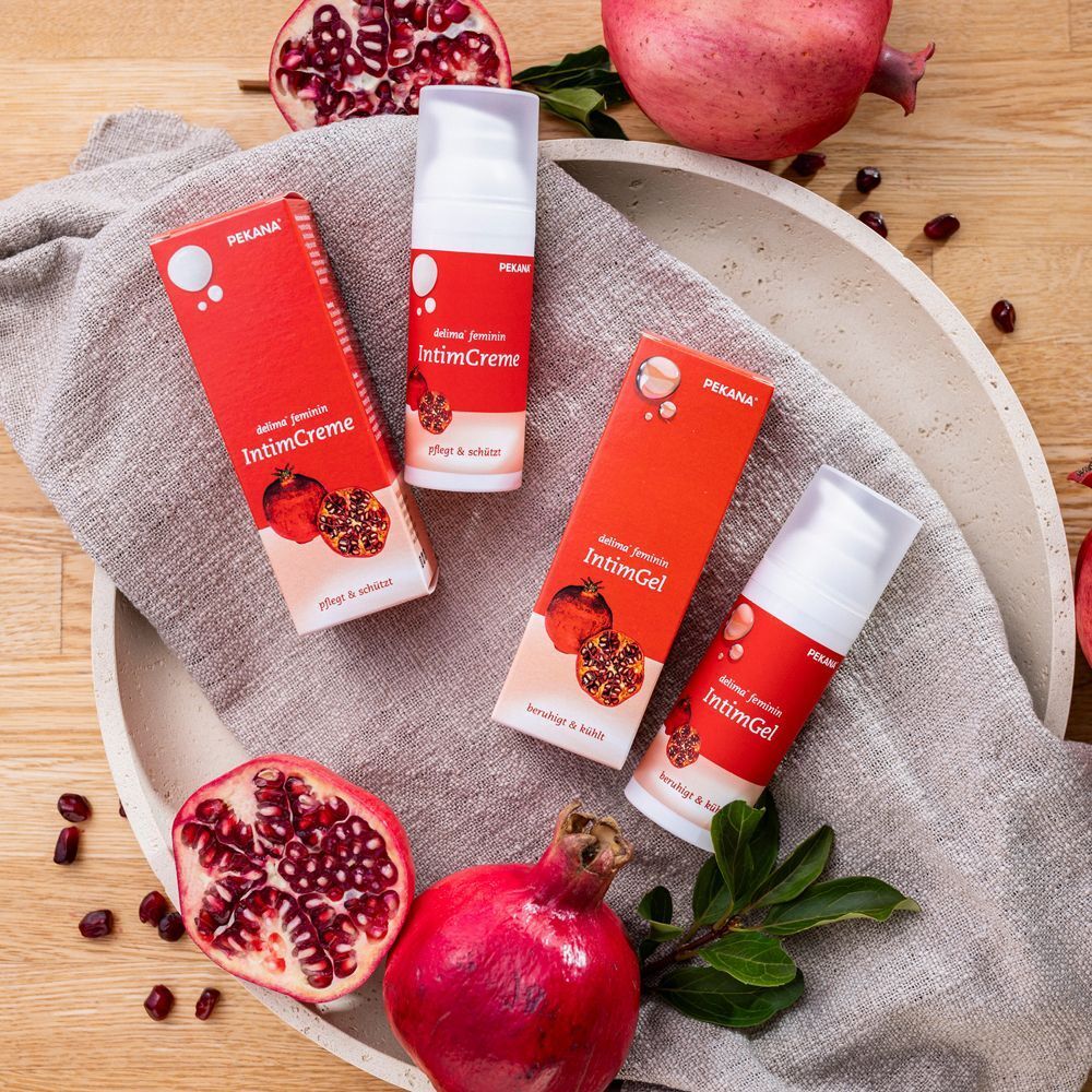 Zwei Flaschen DELIMA feminin IntimGel und zwei IntimCreme mit Granatäpfeln auf einer Servierplatte.
