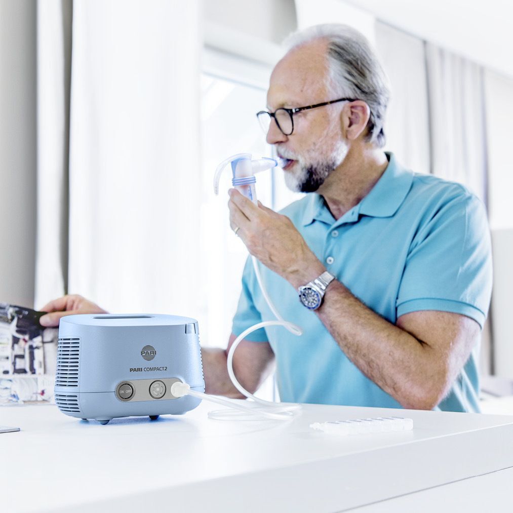 Ein Mann benutzt ein PARI COMPACT 2 Inhalationsgerät. Das Gerät steht auf einem Tisch.
