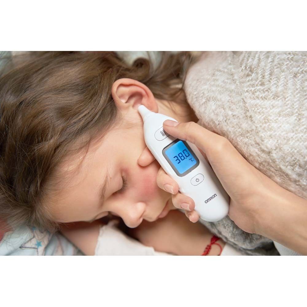 Ohrthermometer am Ohr eines Kindes. Display zeigt 38.0°C. OMRON-Logo.