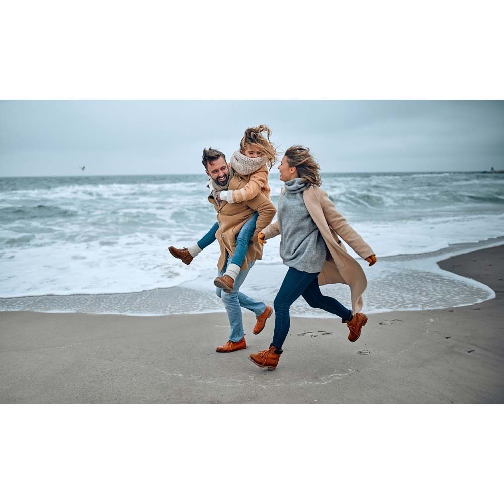Drei Personen laufen am Strand. Ein Mann trägt ein Kind auf dem Rücken, eine Frau läuft daneben.