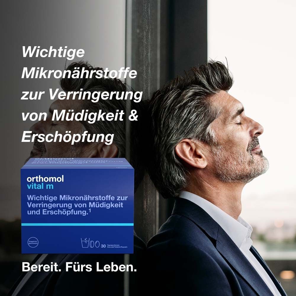 Mann lehnt an Fenster. Im Hintergrund blaue Schachtel Orthomol Vital m. Aufschrift: Wichtige Mikronährstoffe zur Verringerung von Müdigkeit.