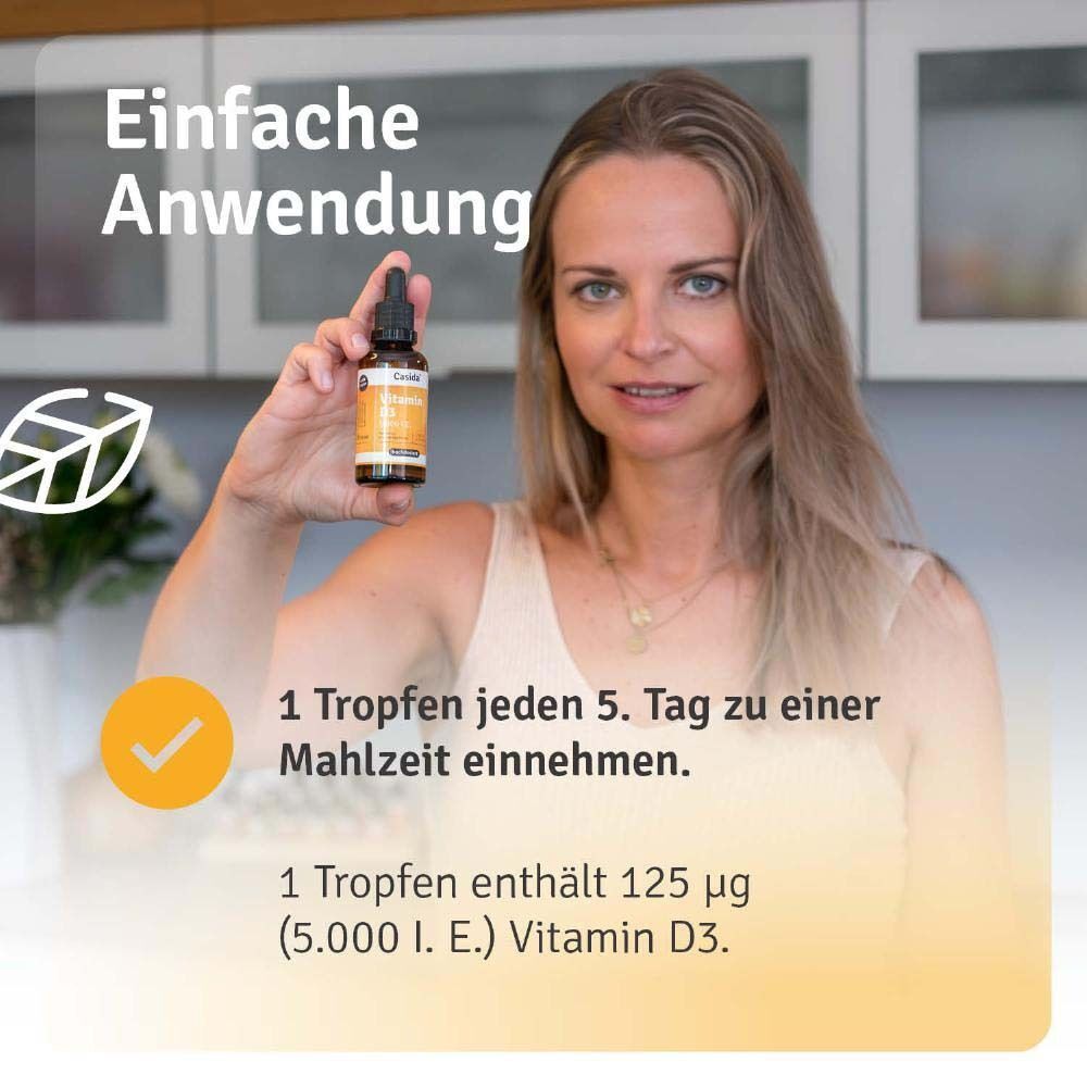 Frau hält Vitamin D3 Tropfen Flasche. Aufschrift: Vitamin D3 5.000 I.E. Casida. Text: 1 Tropfen jeden 5. Tag zu einer Mahlzeit einnehmen.