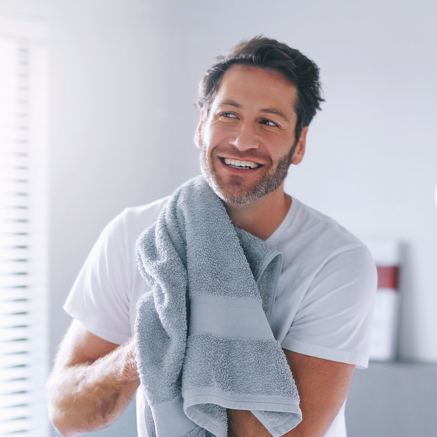 Mann mit Handtuch. Mann lächelt. Hintergrund: Badezimmer.