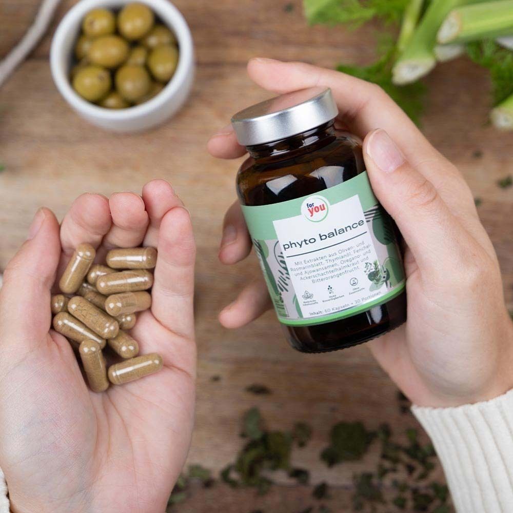 Hände halten eine Braunglasflasche mit 'phyto balance'-Etikett und eine Gruppe von Kapseln.