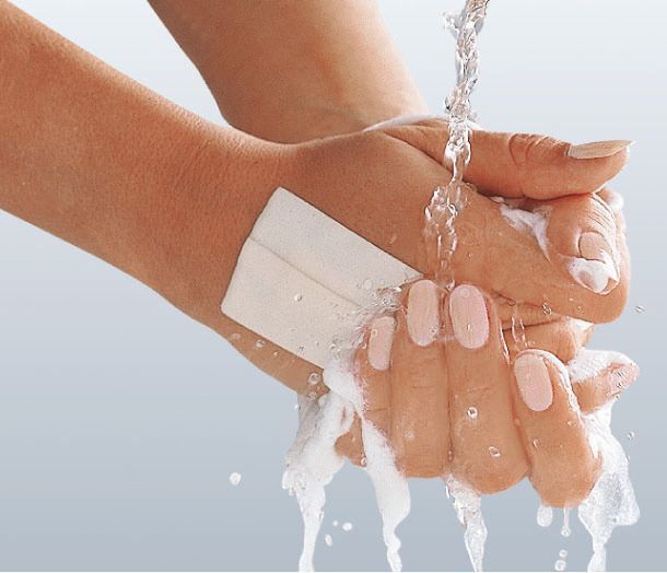 Hände unter fließendem Wasser. Auf einer Hand ist ein weißes Pflaster angebracht.