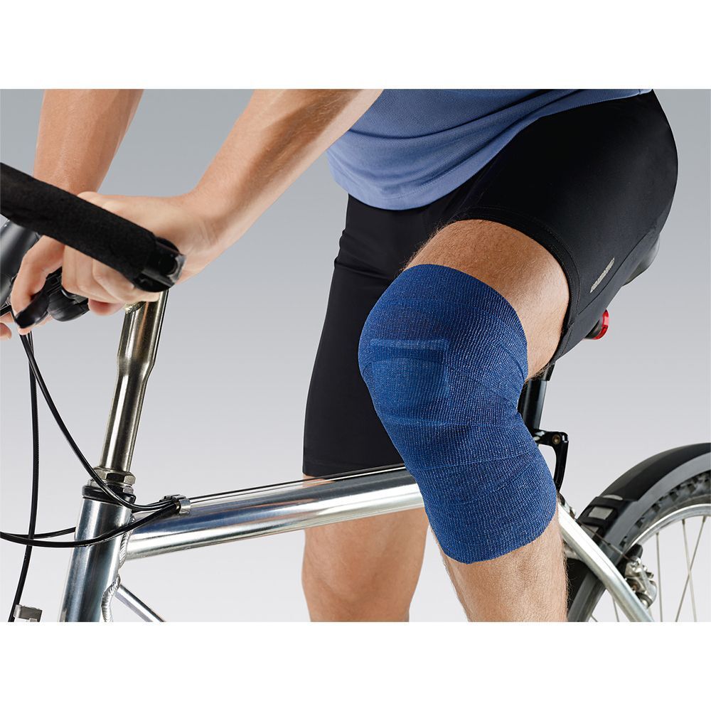 Person mit blauem Verband am Knie, auf Fahrrad sitzend. Verband: blau, rechteckig. Person trägt schwarze Hose.